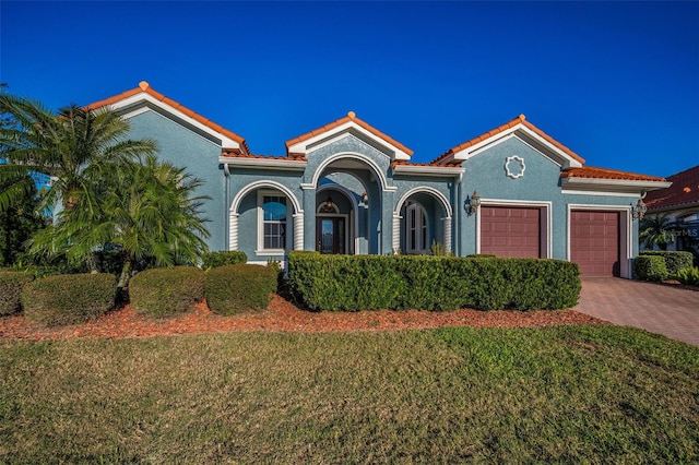 mediterranean / spanish house featuring a garage, a tile roof, a front lawn, and decorative driveway