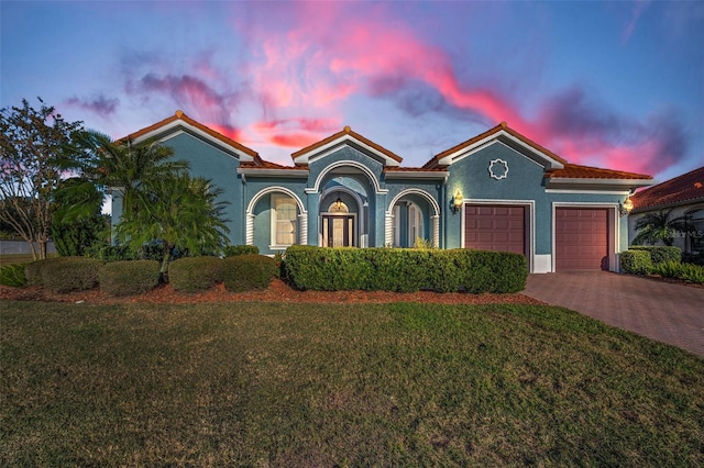 mediterranean / spanish-style house with decorative driveway, stucco siding, a lawn, a garage, and a tiled roof