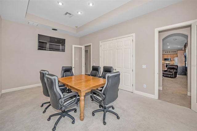 office area with arched walkways, light carpet, visible vents, baseboards, and a tray ceiling