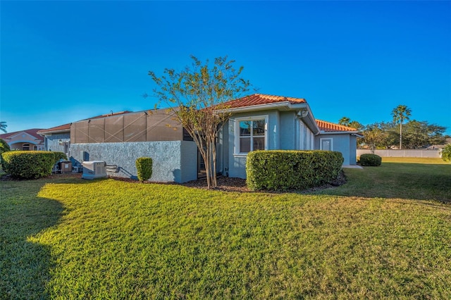 view of side of property featuring cooling unit, a lawn, a tiled roof, and stucco siding