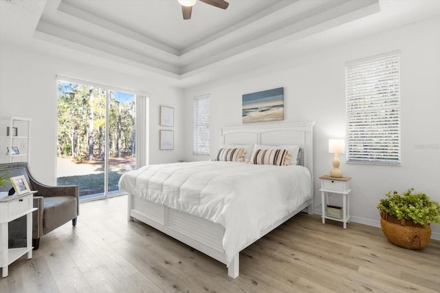 bedroom featuring access to outside, a raised ceiling, and light hardwood / wood-style flooring