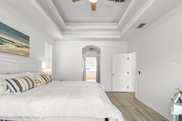 bedroom with ceiling fan, ensuite bathroom, a tray ceiling, and light hardwood / wood-style flooring