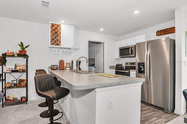 kitchen featuring kitchen peninsula, appliances with stainless steel finishes, sink, white cabinetry, and a breakfast bar