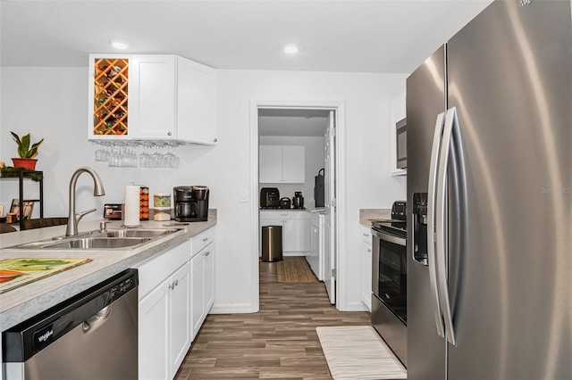 kitchen featuring white cabinets, appliances with stainless steel finishes, washing machine and dryer, dark hardwood / wood-style flooring, and sink