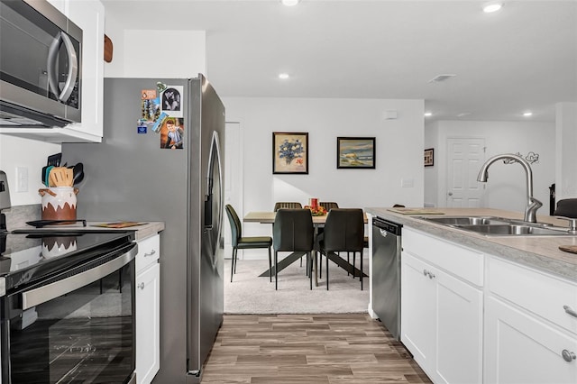 kitchen with sink, wood-type flooring, white cabinets, and stainless steel appliances