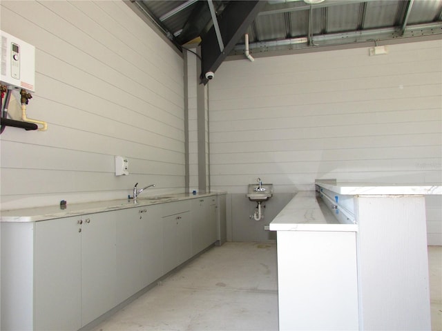 bathroom with wood walls, tankless water heater, concrete flooring, and sink