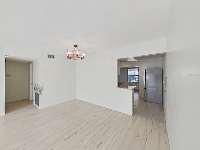 empty room with a chandelier and light wood-type flooring