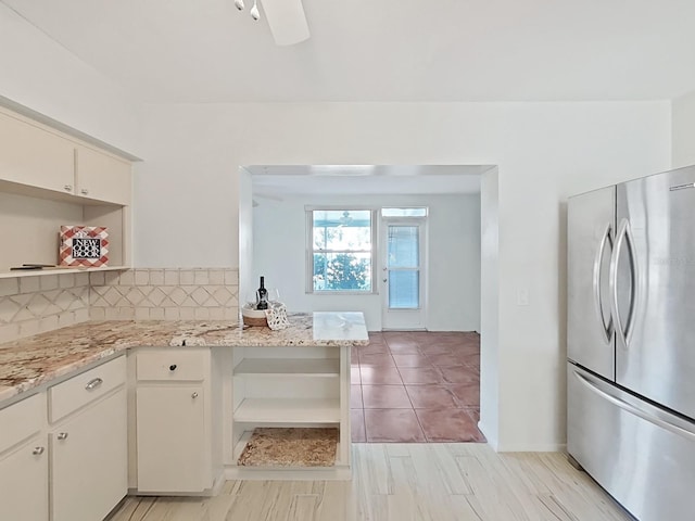 kitchen with kitchen peninsula, tasteful backsplash, light stone counters, ceiling fan, and stainless steel refrigerator