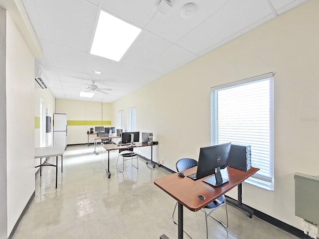 office space with an AC wall unit, ceiling fan, a drop ceiling, and a healthy amount of sunlight