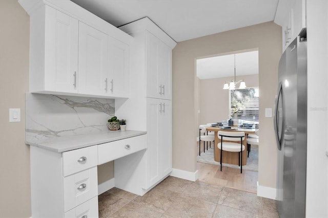 kitchen featuring tasteful backsplash, white cabinets, a chandelier, stainless steel refrigerator, and hanging light fixtures