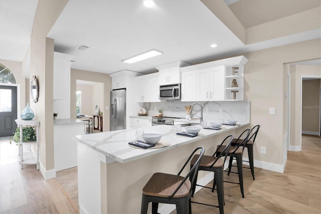 kitchen featuring kitchen peninsula, appliances with stainless steel finishes, a kitchen bar, light hardwood / wood-style flooring, and white cabinetry