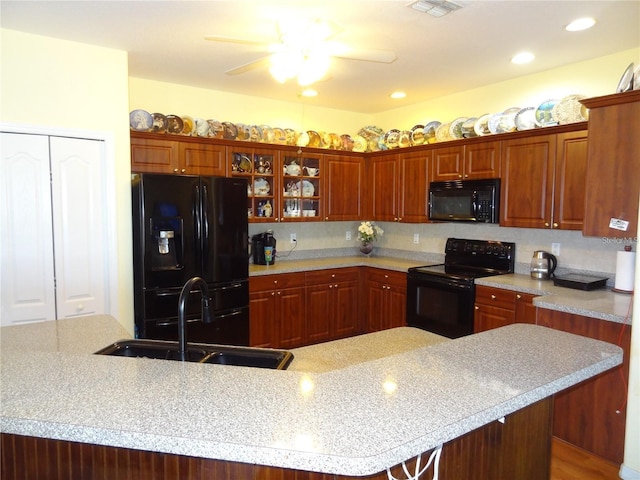 kitchen with ceiling fan, sink, a kitchen breakfast bar, a center island with sink, and black appliances