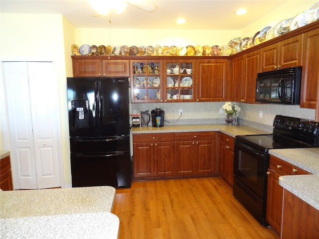 kitchen with black appliances, light hardwood / wood-style flooring, decorative backsplash, ceiling fan, and light stone countertops