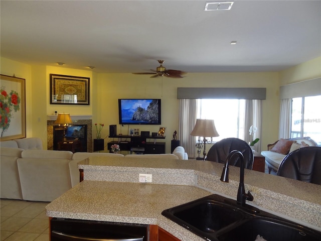 kitchen with ceiling fan, sink, stainless steel dishwasher, a fireplace, and light tile patterned floors