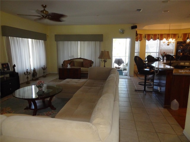 tiled living room with ceiling fan with notable chandelier