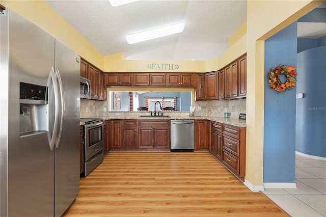 kitchen with sink, stainless steel appliances, light hardwood / wood-style floors, lofted ceiling, and a textured ceiling