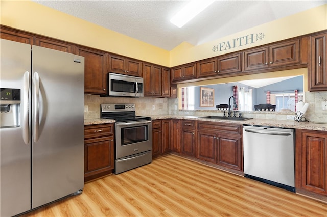 kitchen featuring sink, light hardwood / wood-style flooring, a textured ceiling, vaulted ceiling, and appliances with stainless steel finishes