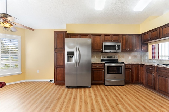 kitchen featuring backsplash, a textured ceiling, stainless steel appliances, ceiling fan, and light hardwood / wood-style floors