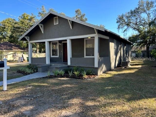 bungalow-style house with a porch, a front lawn, and cooling unit