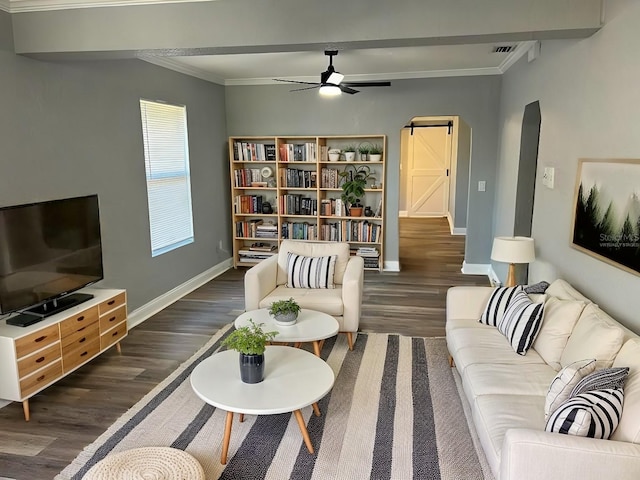 living room with a barn door, ceiling fan, dark wood-type flooring, and ornamental molding