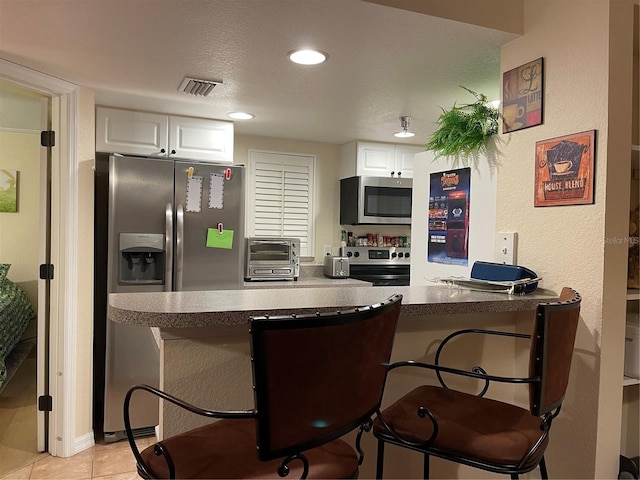 kitchen with light tile patterned floors, white cabinetry, stainless steel appliances, a textured ceiling, and kitchen peninsula