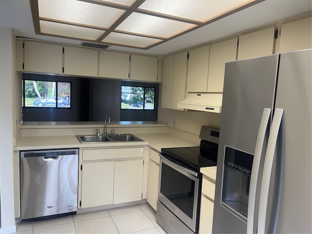 kitchen featuring exhaust hood, cream cabinets, sink, light tile patterned floors, and stainless steel appliances