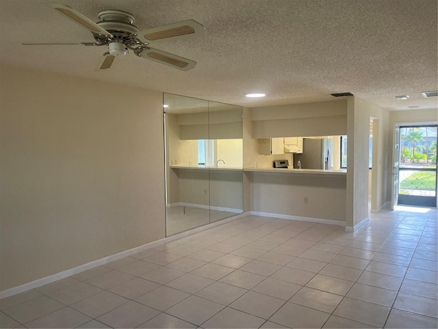 tiled empty room with ceiling fan and a textured ceiling