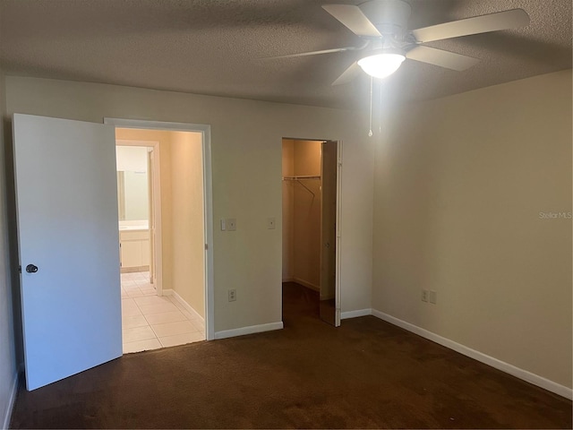 unfurnished bedroom featuring light carpet, ceiling fan, a spacious closet, a textured ceiling, and a closet