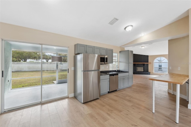 kitchen featuring gray cabinetry, sink, vaulted ceiling, light hardwood / wood-style floors, and stainless steel appliances