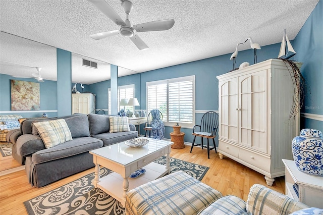 living room with ceiling fan, a textured ceiling, and light wood-type flooring