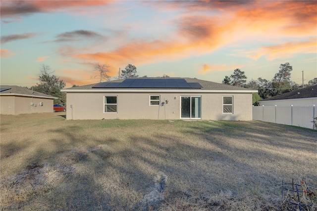 back house at dusk featuring solar panels and a lawn