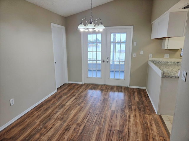 unfurnished dining area featuring french doors, lofted ceiling, an inviting chandelier, and dark wood-type flooring