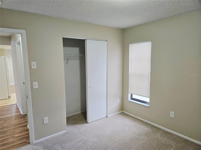 unfurnished bedroom featuring a textured ceiling, white fridge, light carpet, and a closet