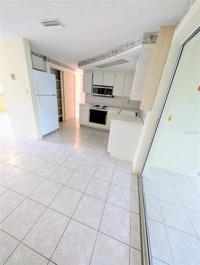 kitchen with white fridge, light tile patterned floors, a textured ceiling, and range with electric cooktop