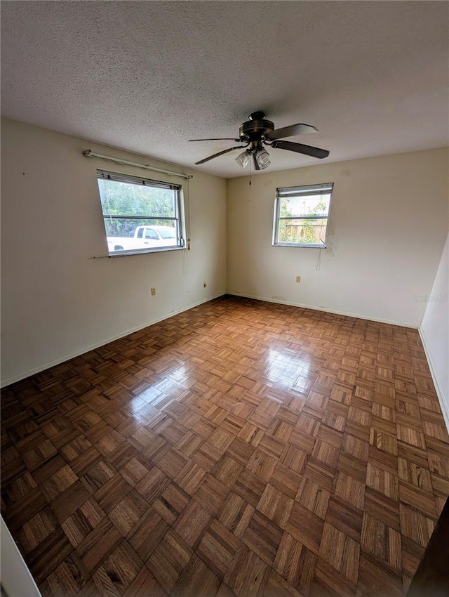 empty room with a textured ceiling, ceiling fan, and dark parquet floors