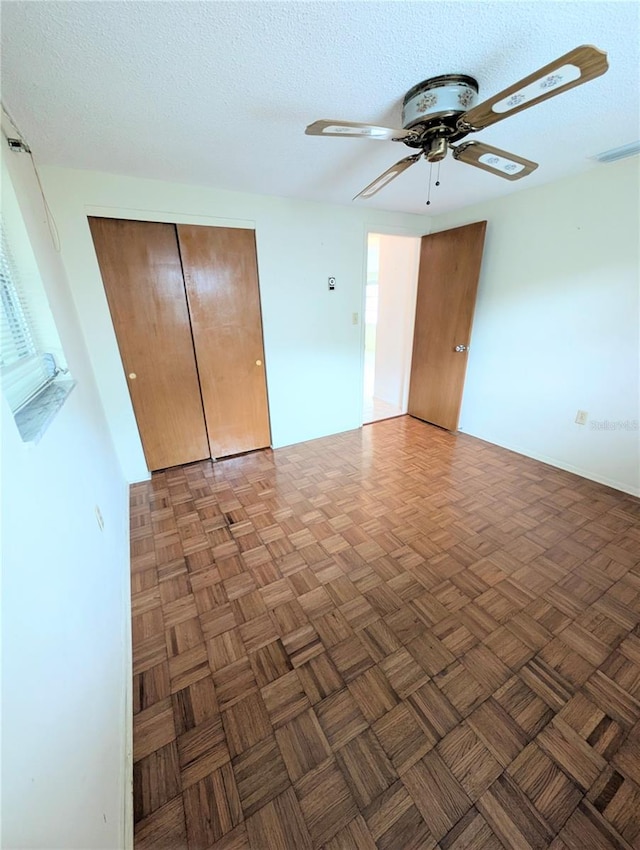 unfurnished bedroom featuring a textured ceiling, ceiling fan, and dark parquet floors