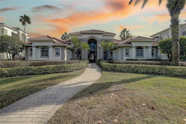 mediterranean / spanish house featuring a garage, a yard, a tiled roof, and stucco siding