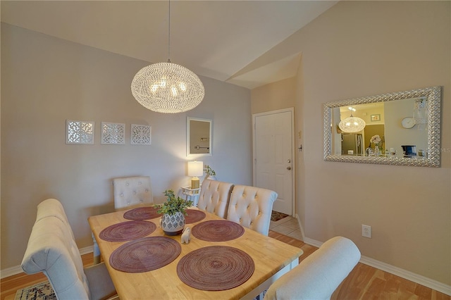 dining space featuring a notable chandelier, light wood-type flooring, and vaulted ceiling