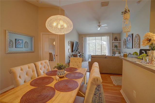 dining area featuring ceiling fan with notable chandelier, light hardwood / wood-style floors, and vaulted ceiling