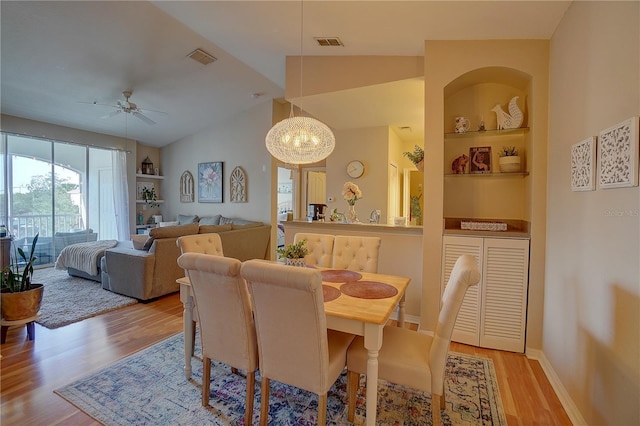 dining area with ceiling fan with notable chandelier, light wood-type flooring, and lofted ceiling