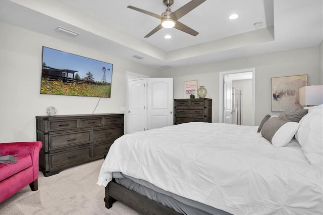 bedroom with ceiling fan, light colored carpet, a tray ceiling, and ensuite bathroom