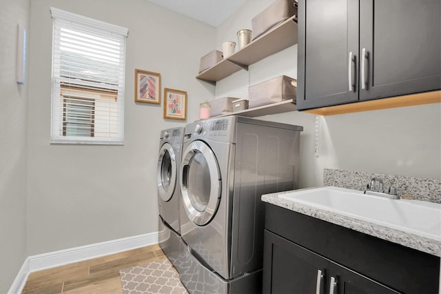 laundry room with cabinets, washer and dryer, light hardwood / wood-style flooring, and sink