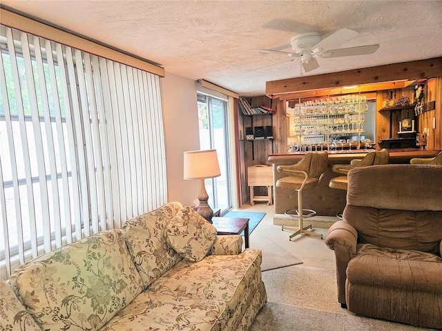 living room featuring ceiling fan, carpet flooring, bar area, and a textured ceiling