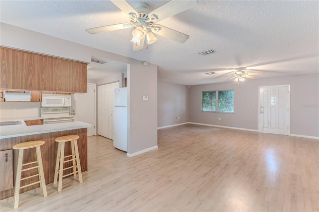 kitchen with white appliances, a textured ceiling, light hardwood / wood-style floors, kitchen peninsula, and a breakfast bar area