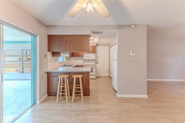 kitchen featuring a kitchen breakfast bar, light hardwood / wood-style floors, white appliances, and kitchen peninsula