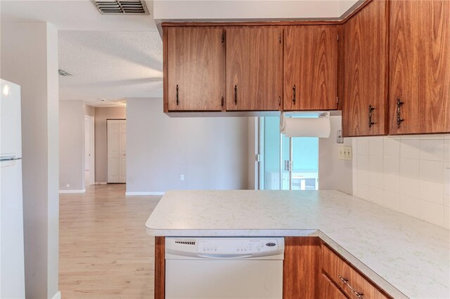 kitchen with light wood-type flooring, a textured ceiling, white appliances, and tasteful backsplash