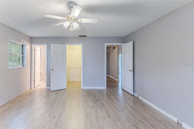 unfurnished bedroom featuring a walk in closet, light hardwood / wood-style flooring, a closet, and ceiling fan