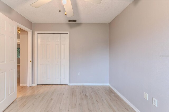 unfurnished bedroom with ceiling fan, a closet, a textured ceiling, and light hardwood / wood-style flooring