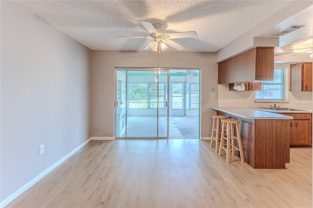 kitchen with ceiling fan, sink, light hardwood / wood-style flooring, kitchen peninsula, and a kitchen bar