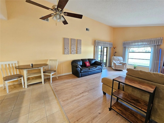 living room featuring ceiling fan, light hardwood / wood-style flooring, high vaulted ceiling, and a textured ceiling